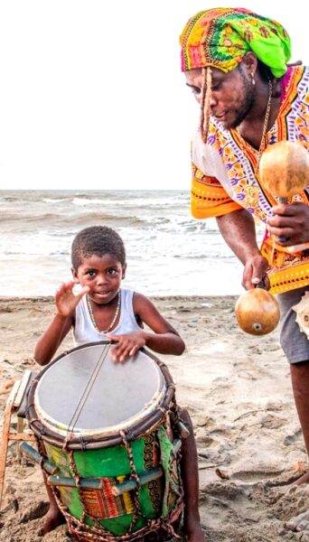A child playing a drum with an older Garifuna musician